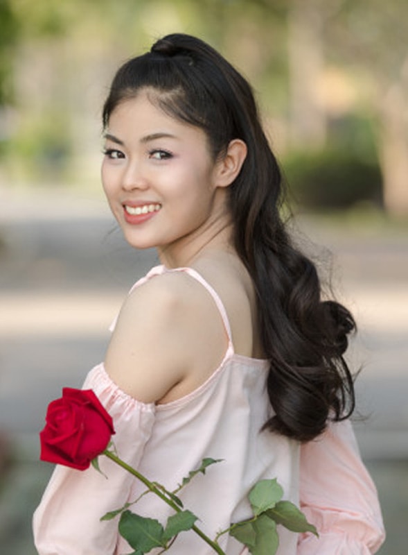 A young Asian woman holding rose behind her back